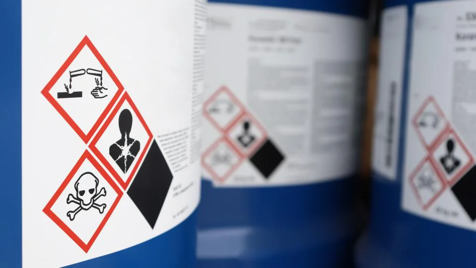 GHS-Gefahrstoffaufkleber mit rot umrandeten Rauten auf Chemikalienbehältern in einem industriellen Lager